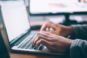 Teksty na stronę internetową - grafika do tekstu. Na obrazku: dłonie człowieka piszącego na laptopie. Autor: Glenn Carstens, źródło: Unsplash.