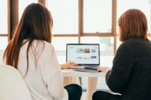 Jak opisać proces współpracy na stronie internetowej? - grafika do tekstu. Na obrazku: dwie kobiety pracujące na laptopie. Autor: Kobu Agency, źródło: Unsplash.